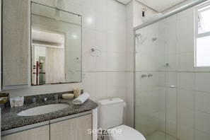 Ein Badezimmer mit Marmorwaschtisch, Toilette, Duschkabine aus Glas und Spiegel über dem Waschbecken.