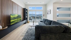Uma sala de estar moderna com uma televisão de tela plana grande, um sofá de cor escura e um armário de madeira.