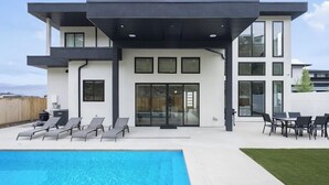 Uma casa moderna de dois andares com piscina, área de estar externa e uma grande porta de vidro deslizante.