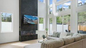 Uma sala de estar moderna com um sofá grande, uma lareira e uma TV fixada na parede.