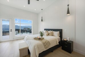 Ein modernes Schlafzimmer mit einem großen Bett, Nachttischen, einer Bank, Blick auf Berge und einer Hängelampe.