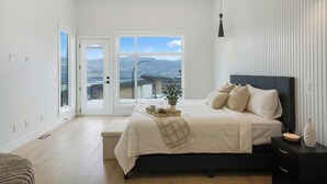 Quarto com uma cama grande, uma mesa de cabeceira, uma luminária e vista para o exterior por uma porta deslizante.