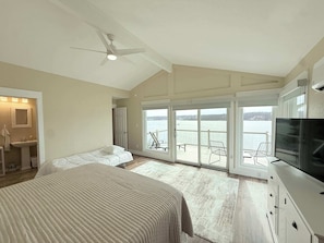 A bedroom with a large bed, a ceiling fan, a TV, and a view of a balcony with a table and chairs. - Sunset Point Lakeview Home Near Margaritaville (Osage Beach)