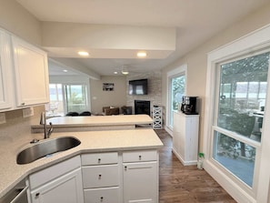 A modern kitchen with granite countertops, white cabinetry, a built-in sink, and a large window offering a view of the outdoors. - Sunset Point Lakeview Home Near Margaritaville (Osage Beach)