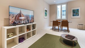 A modern living room with a flat-screen TV, dining table, chairs, and a coffee table. - Palazzo Accademia-Brunelleschi-1 (Firenze)