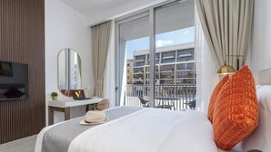 Une chambre d’hôtel comprenant un lit, un bureau, une chaise, une télévision, une fenêtre avec des rideaux et un balcon avec une balustrade.