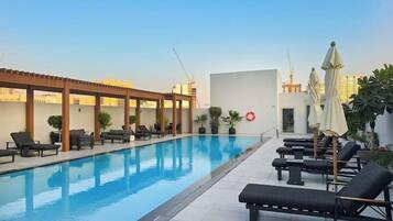 A rooftop swimming pool with lounge chairs and umbrellas, surrounded by potted plants and a pergola.