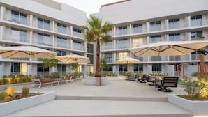 Un hotel de varios pisos con áreas de estar al aire libre, palmeras y sombrillas.