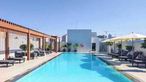 Una piscina en la azotea con sillones de descanso y sombrillas, rodeada por una pérgola de madera y plantas en macetas.