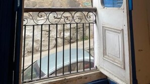 Een kamer met een groot raam, een balkon met metalen hekwerk en uitzicht op een stenen gebouw.