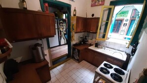Een kleine keuken met houten kastjes, een fornuis en een raam met uitzicht op gebouwen.
