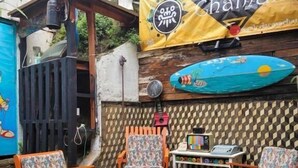 Een terras met houten stoelen en tafels, een surfplank en een banner met tekst.