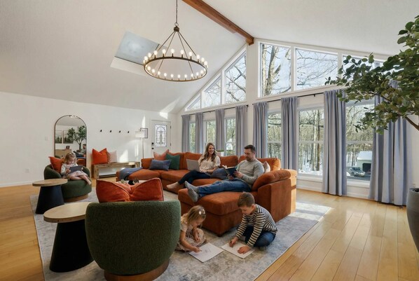 A spacious living room with a high ceiling, large windows, and a chandelier. - The Ridge at Penn Estates | A 4BR Pocono Retreat (East Stroudsburg)