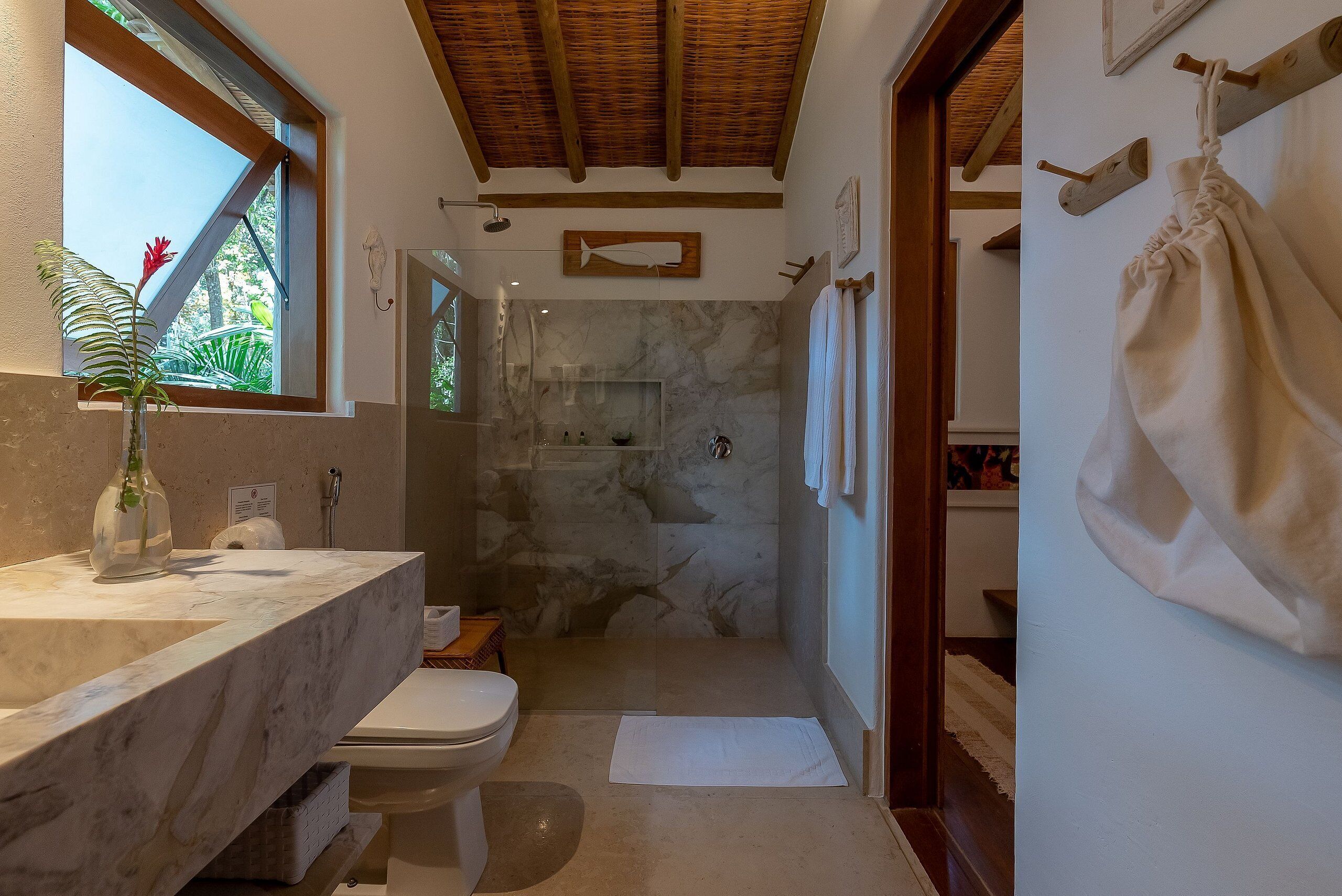 Un baño con lavamanos de mármol, inodoro, ducha con puerta de vidrio y techo de madera.