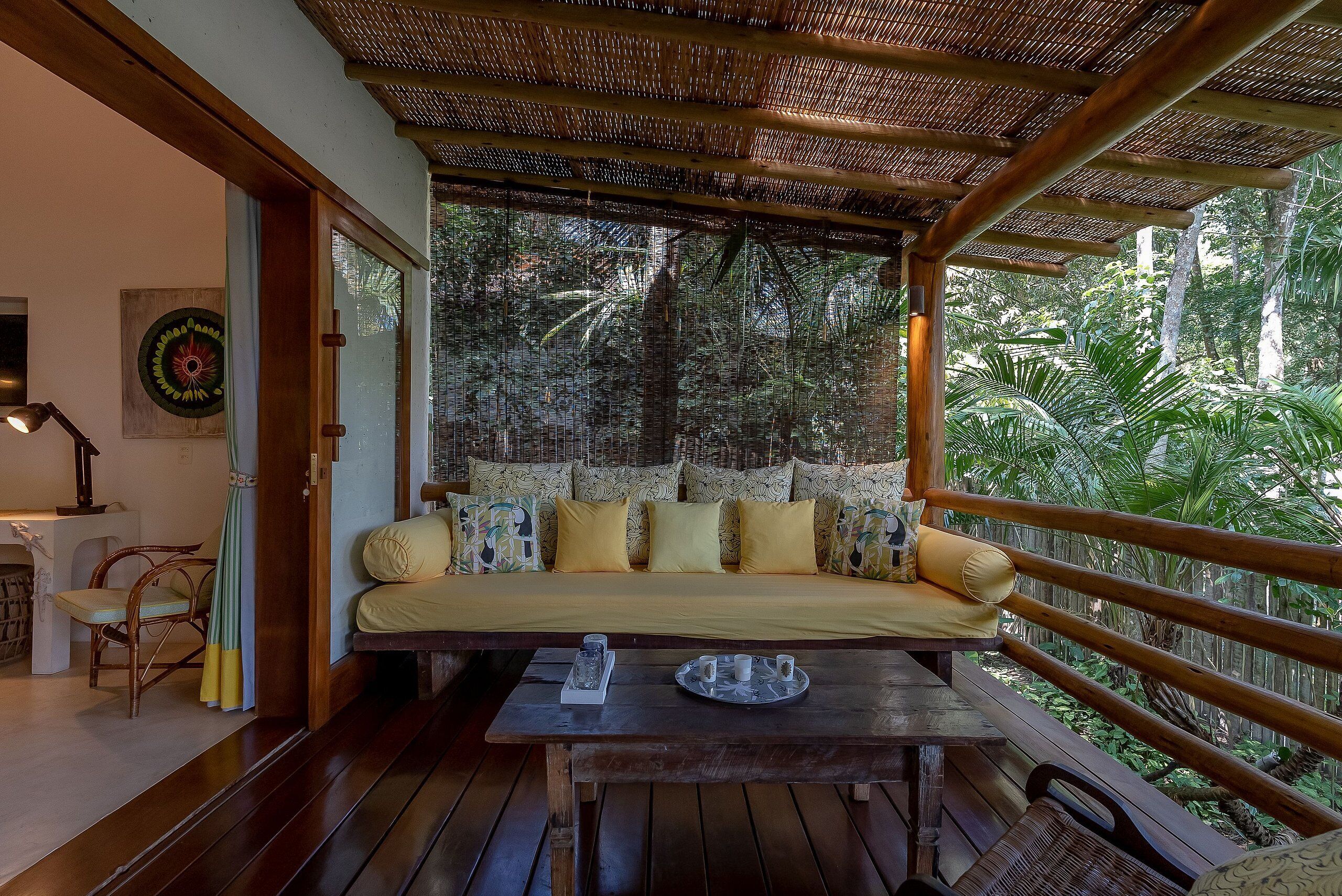 Una terraza de madera con un sofá y una mesa, rodeada de abundante follaje.
