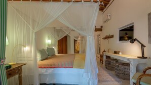 A bedroom with a canopy bed, bedside tables, a desk, and wicker ottomans. - 142D Casa com 03 Suítes em Trancoso (Porto Seguro)