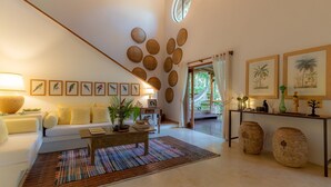 A living room with a sofa, coffee table, and wall-mounted decorations. - 142D Casa com 03 Suítes em Trancoso (Porto Seguro)