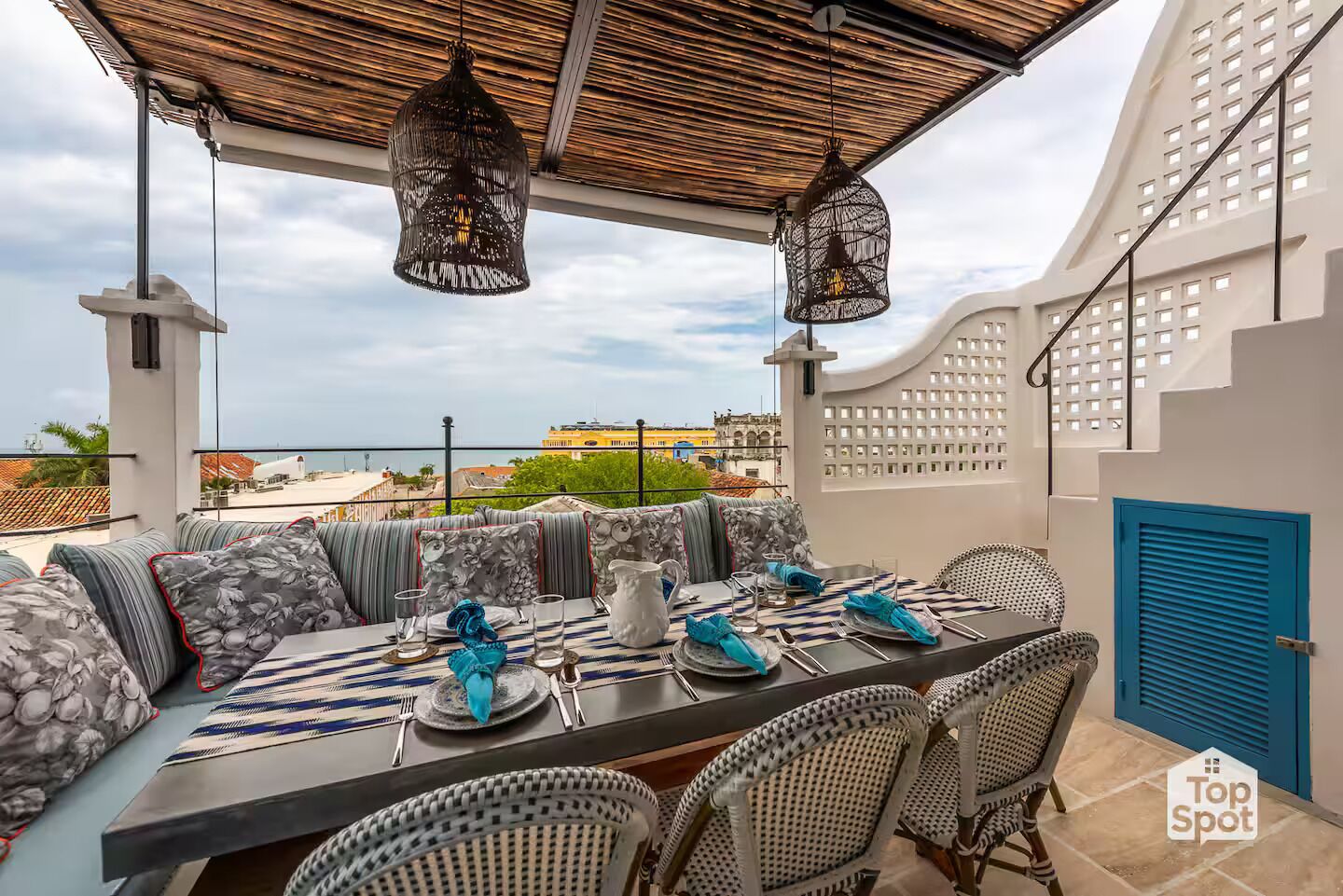 Een terras met een eettafel voor vier personen, omringd door rieten stoelen, onder een rieten dak.