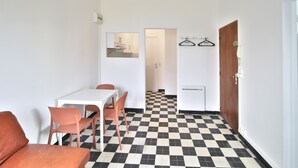Una habitación compacta con piso a cuadros, una mesa blanca con sillas, una puerta de madera y un perchero.