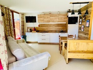 A compact living space with a sofa, dining table, kitchenette, and a TV mounted on the wall. - Marvel Morillon - 10 min de la station (Morillon)
