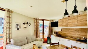 A cozy living room with a sofa, a wooden dining table, and a kitchen area with cabinets and a TV. - Marvel Morillon - 10 min de la station (Morillon)