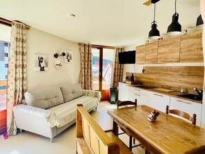 A cozy living room with a sofa, a wooden dining table, and a kitchen area with cabinets and a TV. - Marvel Morillon - 10 min de la station (Morillon)