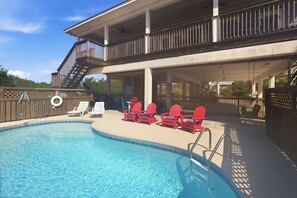 Ein Swimmingpool mit überdachtem Deckbereich, roten Stühlen und einer Treppe zu einer erhöhten Ebene.