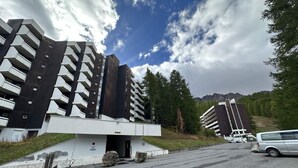 Un bâtiment moderne doté de nombreux balcons, d’un espace de stationnement et surplombant un paysage montagneux.
