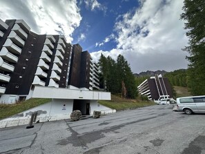 Ein modernes Gebäude mit mehreren Balkonen, einem Parkplatz und einer Bergkulisse.