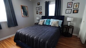 A bedroom with a large bed, two bedside tables, a window with curtains, and several framed pictures on the wall. - Cute 4 Bed house - Central Tulsa with Fenced back yard (Tulsa)