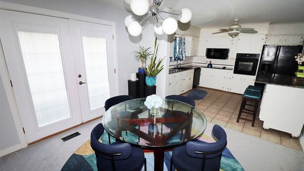A modern kitchen with white cabinets, a black refrigerator, and a dining area with a glass table and blue chairs. - Cute 4 Bed house - Central Tulsa with Fenced back yard (Tulsa)