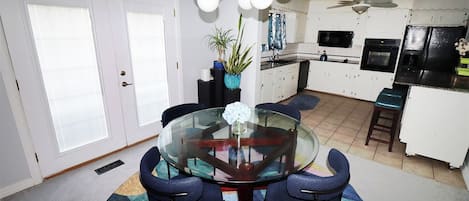 A modern kitchen with white cabinets, a black refrigerator, and a dining area with a glass table and blue chairs.