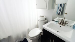 A bathroom with a toilet, a sink with a mirror, and a towel rack. - Cute 4 Bed house - Central Tulsa with Fenced back yard (Tulsa)