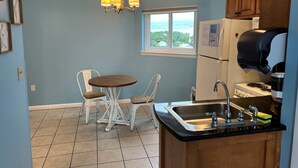 A kitchen with a dining area, a window with a view, and a refrigerator. - Cozy Corner Studio Unit - Perfect for 2! (Gulf Shores)