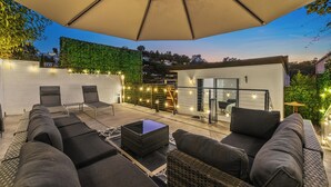 Eine Terrasse im Freien mit einem großen Sonnenschirm, Korbmöbeln und Lichterketten.