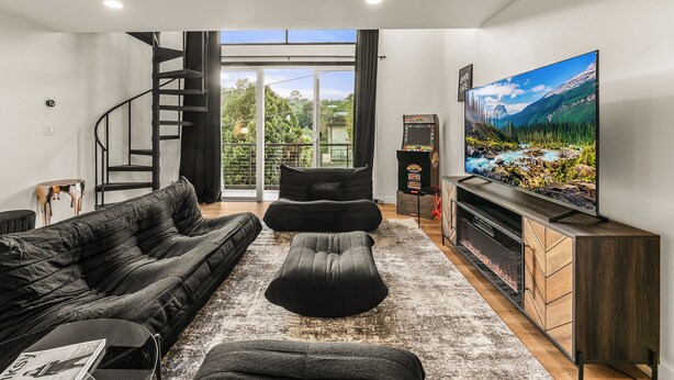 Ein modernes Wohnzimmer mit einem schwarzen Sofa, einem Hocker und einem großen Flachbildfernseher auf einer Holzkommode.