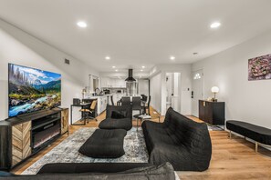 A modern living room with a large flat-screen TV, black sofas, and a wooden entertainment unit.