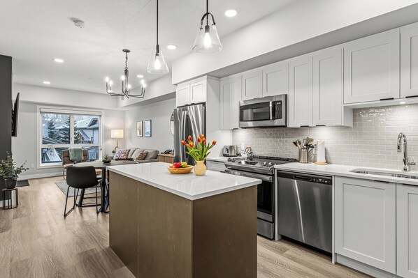 A modern kitchen with white cabinets, stainless steel appliances, and a central island with a vase of tulips. - Stylish, Modern One Bedroom Suite on the Second Level. Pool, Gym and Hot Tub! (Dead Man's Flats)