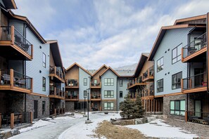 A multi-story residential building with balconies, a central courtyard, and a snow-covered ground. - Stylish, Modern One Bedroom Suite on the Second Level. Pool, Gym and Hot Tub! (Dead Man's Flats)