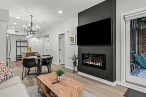 A modern living room with a fireplace, a dining area, and a kitchen in the background. - Stylish, Modern One Bedroom Suite on the Second Level. Pool, Gym and Hot Tub! (Dead Man's Flats)