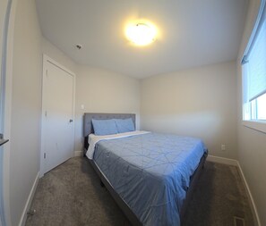A bedroom with a bed, a door, a window, and a ceiling light.