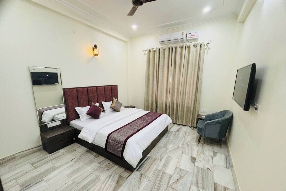 A hotel room with a bed, a TV, a ceiling fan, an air conditioning unit, and a window with curtains.