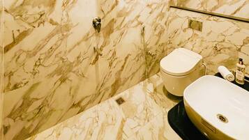 A bathroom with a marble wall, a toilet, a sink, and a towel dispenser.