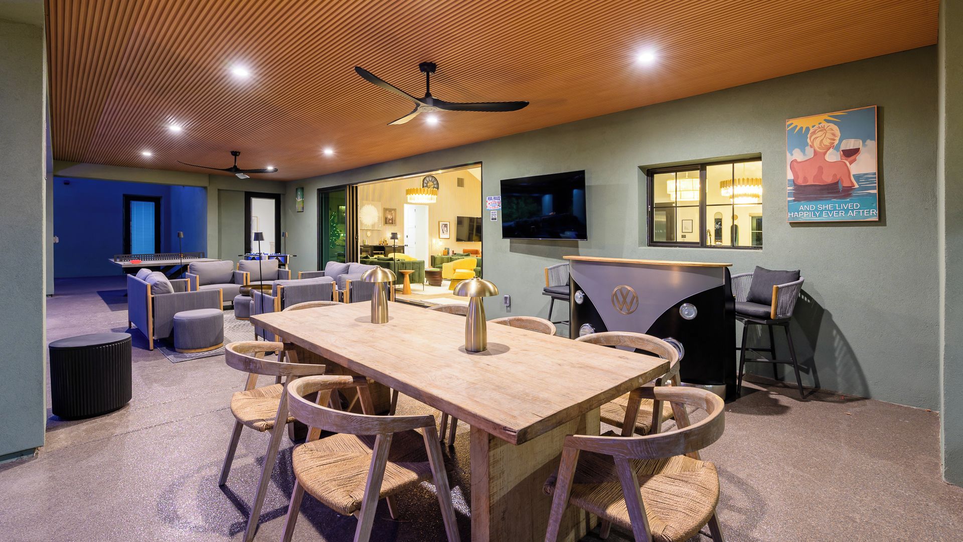 A room with a wooden table and chairs, a bar area, and a television.