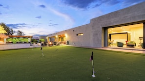 A modern outdoor area with a putting green, a covered seating area, and a building entrance. - Luxury 5BR Scottsdale Villa: Pool, Spa, Pickleball, Golf Simulator, Gym and More (Scottsdale)