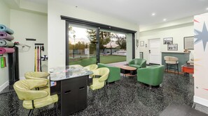 A room with green chairs, a foosball table, and a window overlooking a tennis court. - Luxury 5BR Scottsdale Villa: Pool, Spa, Pickleball, Golf Simulator, Gym and More (Scottsdale)