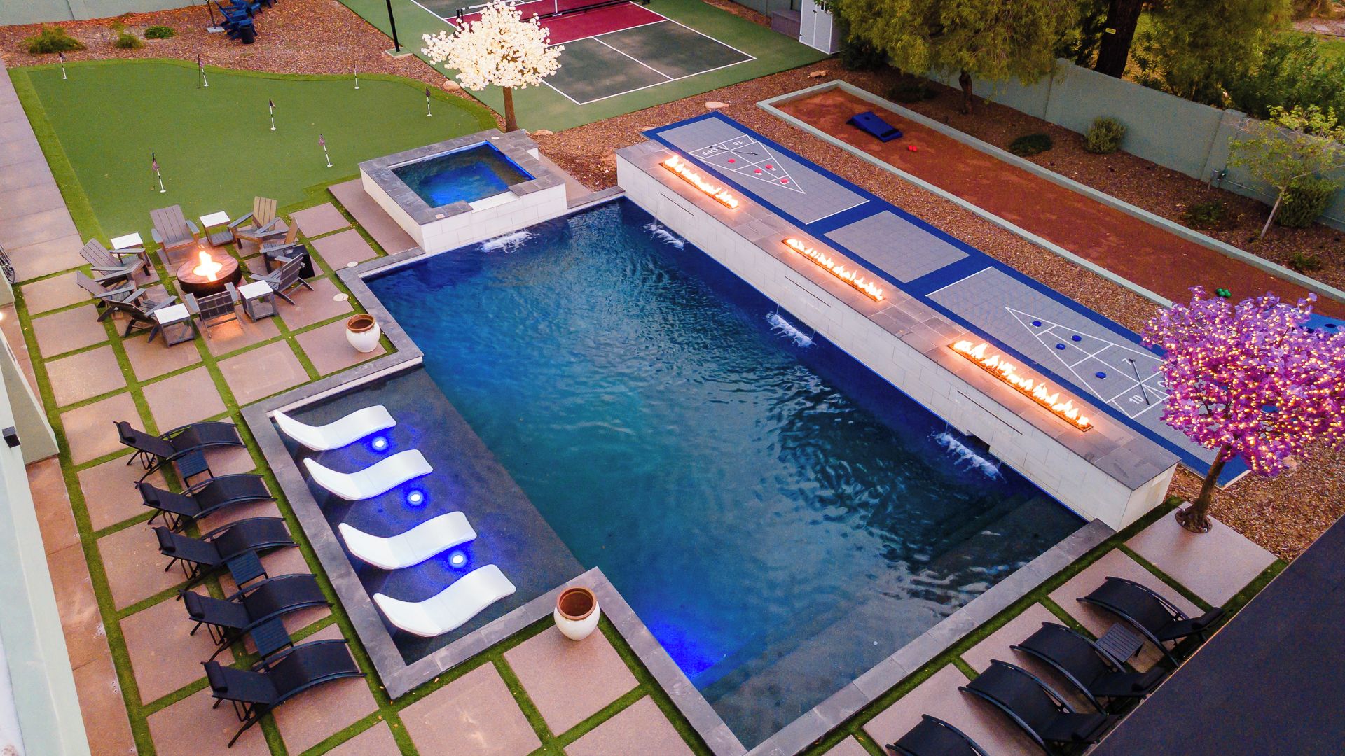 A swimming pool with a fire feature, lounge chairs, and a shuffleboard area.