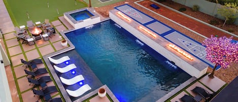 Una piscina con una chimenea, sillas de descanso y una zona para jugar a pala.'