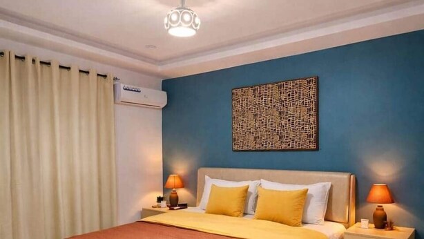 Une chambre à coucher comprenant un lit, des tables de chevet, un climatiseur fixé au mur et un luminaire au plafond.
