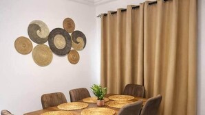 Un coin repas avec une table en bois, six chaises et un rideau.